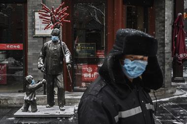 A protective mask is seen on statues outside a restaurant as a guard wearing a protective mask walks by in an empty and shuttered commercial street on February 5, 2020 in Beijing, China