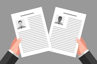 An image showing the hands of a white man holding the CVs of two applicants, a white one and a black one