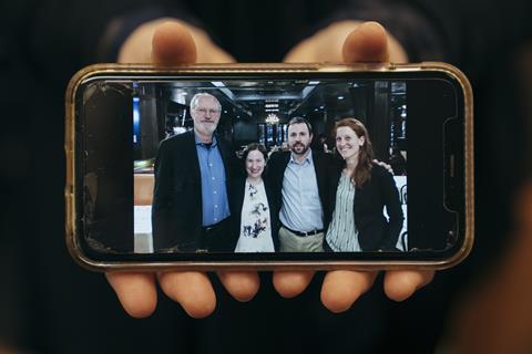 Hands holding a phone showing a photograph of Melanie Sanford and mentors, including Bob Grubbs